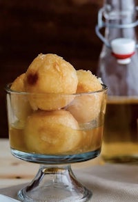 a bowl of fried doughnuts next to a bottle of honey