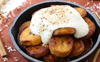 a bowl of fried bananas topped with cream and cinnamon